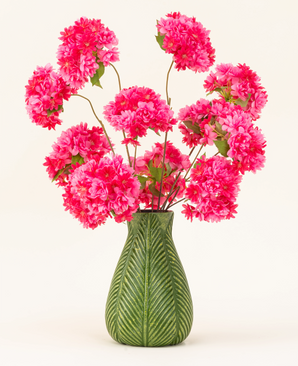 Een groene vaas met bladmotief toont het Zijden kunstbloemen boeket Kersenbloesem Roze-helderroze, pluizige zijden kersenbloesems met groene bladeren-tegen een effen lichte achtergrond.