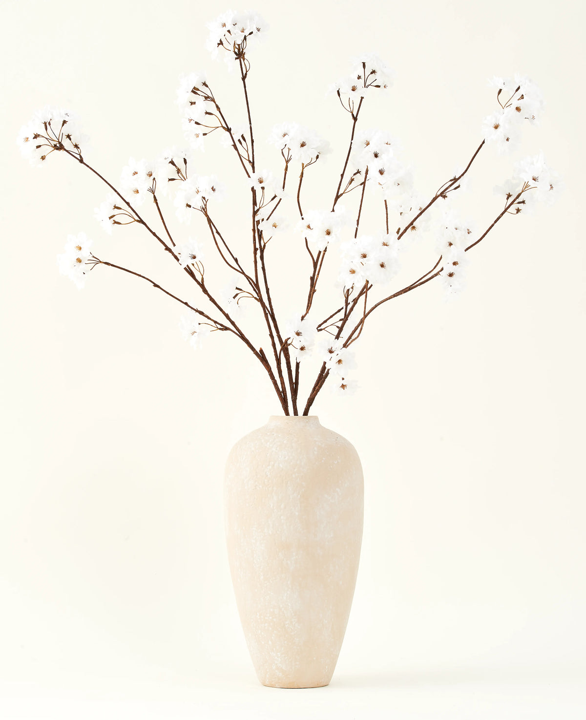 Het Zijden kunstbloemen boeket Kersenbloesem crème 114 cm staat hoog in een beige keramische vaas en brengt een serene decoratie in elke ruimte met zijn delicate, crèmekleurige takken tegen een lichte achtergrond.