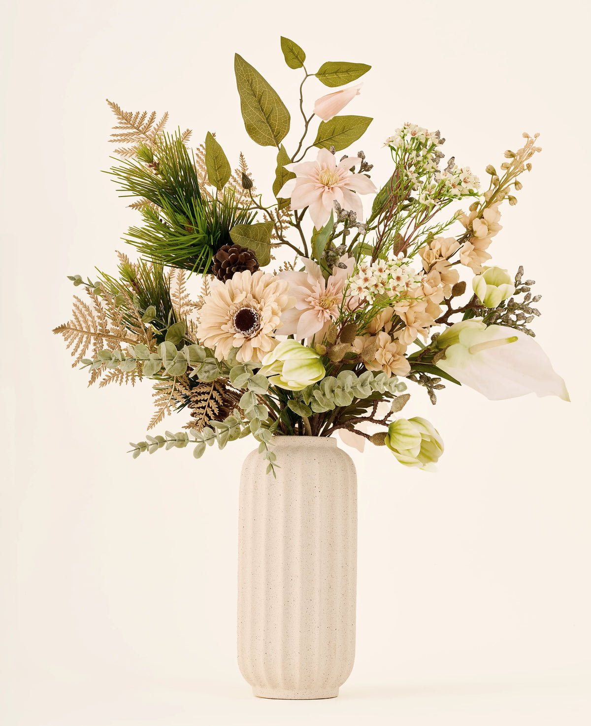Zijden kunstbloemenboeket Golden Winter, bestaande uit kunstbloemen, bladgroen en een dennenappel in een geribbelde, gebroken witte vaas.
