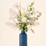 Zijden kunstbloemenboeket Silent Night, bestaande uit witte rozen en calla’s in een hoge, geribbelde blauwe vaas.