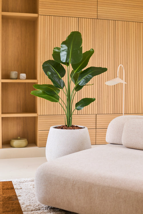 Kunstplant Strelitzia 150 cm: een levensechte kunstplant met brede groene bladeren in een gespikkelde, ronde plantenbak.