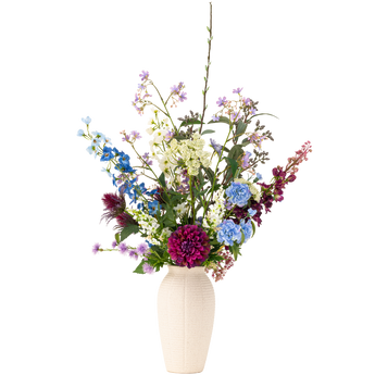 Een crèmekleurige vaas bevat een bloemstuk van verschillende bloemen, waaronder blauwe, paarse, bordeauxrode en witte bloemen met groen gebladerte, tegen een effen witte achtergrond.