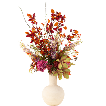 Een crèmekleurige vaas bevat een arrangement van herfstige bloemen en bladeren in rode, oranje, paarse, groene en witte tinten tegen een witte achtergrond.