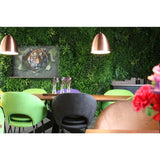 Een moderne eethoek met groene en perzikkleurige stoelen, een tafel versierd met vazen met paarse bloemen, koperen hanglampen, een weelderige plantenwand gemaakt met het Kunsthaag Crush UV-paneel van 100 x 100 cm, en op de achtergrond een ingelijste afbeelding van een tijger.