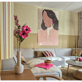 Een moderne woonkamer met een modulaire bank, een roze bloemstuk van Kunstbloem Catnip (75 cm) in een vaas, een donzige plaid en een abstract wandschilderij van een vrouw. Het interieur wordt gekenmerkt door zachte kleuren en accenten met patronen.