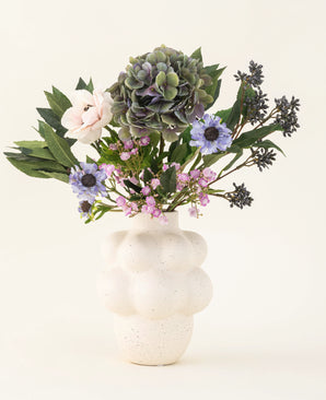 In een witte vaas met structuur staat het Zijden kunstbloemen boeket Blue Belle - met hortensia's, margrieten, roze rozen en meer - tegen een effen lichte achtergrond.