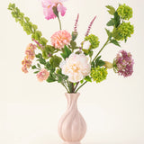 Het Zijden kunstbloemen boeket First Light heeft witte, roze, groene en paarse bloemen met groene bladstelen in een pastelroze vaas - een elegant accent voor elke ruimte.