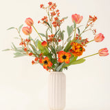 Het Zijden kunstbloemen boeket Orange Glory, met oranje tulpen, klaprozen en groene bladeren, is prachtig gerangschikt in een vaas met witte textuur tegen een effen lichte achtergrond.