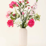 Een vaas met witte textuur toont het Zijden kunstbloemen boeket Blush Breeze - roze, witte en lichtpaarse zijden bloemen met groene bladeren - tegen een effen lichte achtergrond.