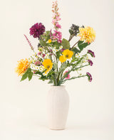 Het Zijden kunstbloemen boeket Daisy Daydream heeft een vaas met witte textuur en een levendige mix van gele, roze, paarse en witte bloemen met groene bladeren, die blijvende schoonheid toevoegt aan elke effen lichte achtergrond.