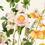 Een close-up van het Zijden kunstbloemen boeket Blossom Harmony, met een roze margrietachtige bloem met een geel hart, omringd door lichtroze bloesems en oranje-gele orchideeën, tegen een lichte achtergrond.