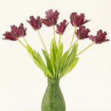 De Zijden kunstbloemen boeket Franse Parkiet Tulp paars heeft donkerpaarse, gefranjerde tulpen met lange groene stelen in een vaas met groen bladmotief, waardoor een opvallende display tegen een witte achtergrond ontstaat.