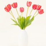 De Zijden kunstbloemen boeket Franse Tulp rood is gerangschikt in een vaas van wit keramiek, met acht rode en gele tulpen met groene bladeren tegen een effen lichte achtergrond.