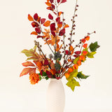 Een vaas met witte structuur toont het Zijden kunstbloemen boeket Chestnut Charm, met herfstbladeren, oranje bloemen en groen gebladerte - een elegant kunstarrangement tegen een effen lichte achtergrond.