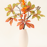 Het Zijden kunstbloemen boeket Herfst Flair heeft een vaas met witte structuur en lampiontak, oranje lampionvormige bloemen en groenrode bladeren, die een stijlvolle herfsttentoonstelling vormen tegen een effen lichte achtergrond.