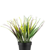 De Kunstplant Grasplant in pot UV 26 cm heeft lange groene en paarse bladeren met kleine witte bloemen, gerangschikt in een eenvoudige zwarte pot en weergegeven tegen een witte achtergrond.