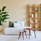 Minimalistische woonkamer met een witte bank, twee kussens, houten nesttafels en een grote Kunstplant Strelitzia Real Touch Deluxe 180 cm voor een tropische sfeer. Een moderne open houten boekenplank met vazen staat tegen de beige muur.