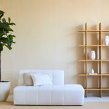 Minimalistische woonkamer met een witte bank, twee kussens en een Kunstplant Ficus Tabaksplant Deluxe 180 cm naast een open houten plank met witte vazen, alles tegen een beige muur en op een licht vloerkleed.