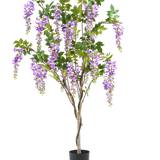De Kunstplant Blauweregen 150 cm is een kunst blauwe regen in pot met groene bladeren en paarse bloemen, tegen een effen witte achtergrond.