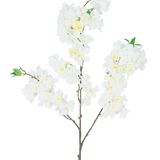 De Kunst Kersenbloesem 106 cm wit heeft een enkele bruine tak met trosjes witte kunstkersenbloesembloemen en kleine groene blaadjes, tegen een effen witte achtergrond.