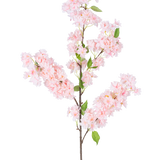 De Kunst Kersenbloesem 100 cm roze heeft een lange bruine steel, trossen lichtroze kersenbloesem bloemen en groene bladeren tegen een witte achtergrond.