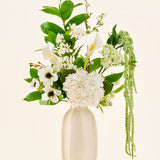 In een witte keramische vaas staat het boeket ‘Green Elegance’ van Zijden kunstbloemen, een arrangement van witte hortensia’s, calla’s, anemonen, groene bladeren en hangend groen tegen een effen lichte achtergrond.