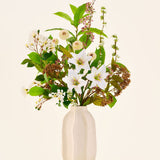 Zijden kunstbloemenboeket Timeless Bloom, bestaande uit een boeket van diverse witte lelies, kleine witte bloemen en groen in een beige vaas met structuur.