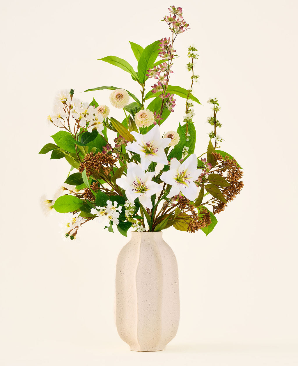 Zijden kunstbloemenboeket Timeless Bloom, bestaande uit een boeket van diverse witte lelies, kleine witte bloemen en groen in een beige vaas met structuur.