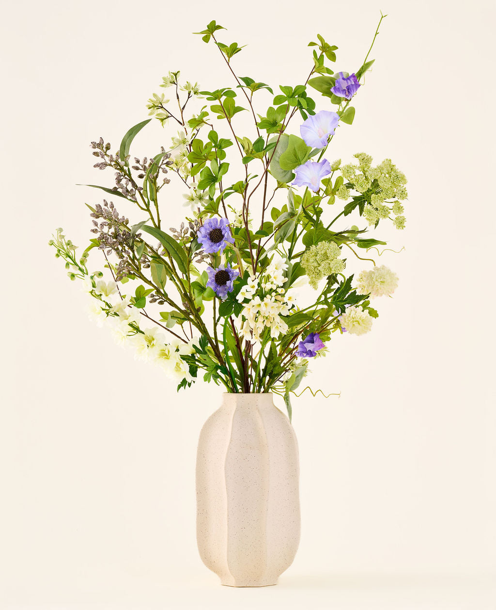 Zijden kunstbloemenboeket Forest Light met paarse, groene en witte bloemen, geschikt in een structuurrijke, gebroken witte vaas.