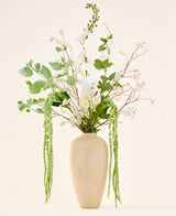 Een boeket van zijden kunstbloemen, Crystal Garden, bestaande uit witte en groene bloemen en hangend blad in een hoge, beige vaas met structuur.
