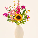 In een beige keramische vaas staat het zijden kunstbloemenboeket ‘Tiny Sunshine’, bestaande uit een kunstboeket van levensechte bloemen, zoals een grote zonnebloem, roze en magenta bloesems en gele bloemen met groen blad, tegen een effen lichte achtergrond. Dit arrangement van Easyplants bestaat uit prachtige zijden bloemen die elke ruimte langdurige schoonheid verlenen.