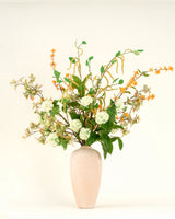 Een beige vaas van keramiek bevat het Zijden kunstbloemen boeket Golden Meadow, met groene bladeren, witte hortensia-achtige bloemen en oranje bloesems tegen een effen witte achtergrond.