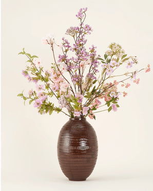In een vaas met bruine structuur staat het Zijden kunstbloemen boeket Lilac, met roze, paarse en witte bloemen met groen bladgroen, natuurlijk gerangschikt tegen een effen lichte achtergrond.