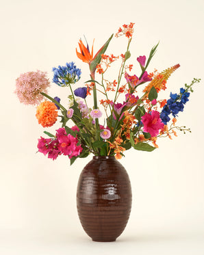 In een donkere vaas met textuur staat het Zijden kunstbloemen boeket Tropical Firework, een kleurrijke mix van oranje, roze, paarse, blauwe en gele zijden bloemen, gerangschikt voor blijvende schoonheid tegen een effen lichte achtergrond.
