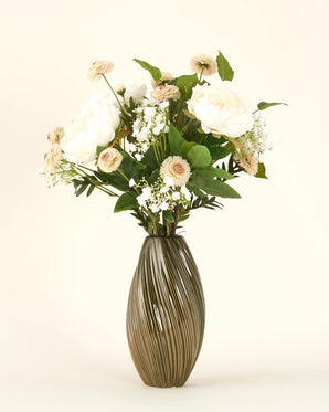 Het Zijden kunstbloemen boeket White Love heeft witte en lichtroze bloemen met groen gebladerte in een geribbelde vaas van keramiek, prachtig gerangschikt tegen een effen lichte achtergrond.