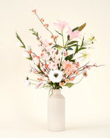 Het Zijden kunstbloemen boeket Pink & Pearl staat in een beige vaas van keramiek, met delicate roze, witte en perzikkleurige bloemen met groen gebladerte tegen een licht crèmekleurige achtergrond.