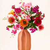 In een perzikkleurige vaas staat het boeket „Tropical Sunset“ van Zijden kunstbloemen, bestaande uit een levendige mix van roze, oranje, gele en rode bloemen tegen een effen, lichte achtergrond.
