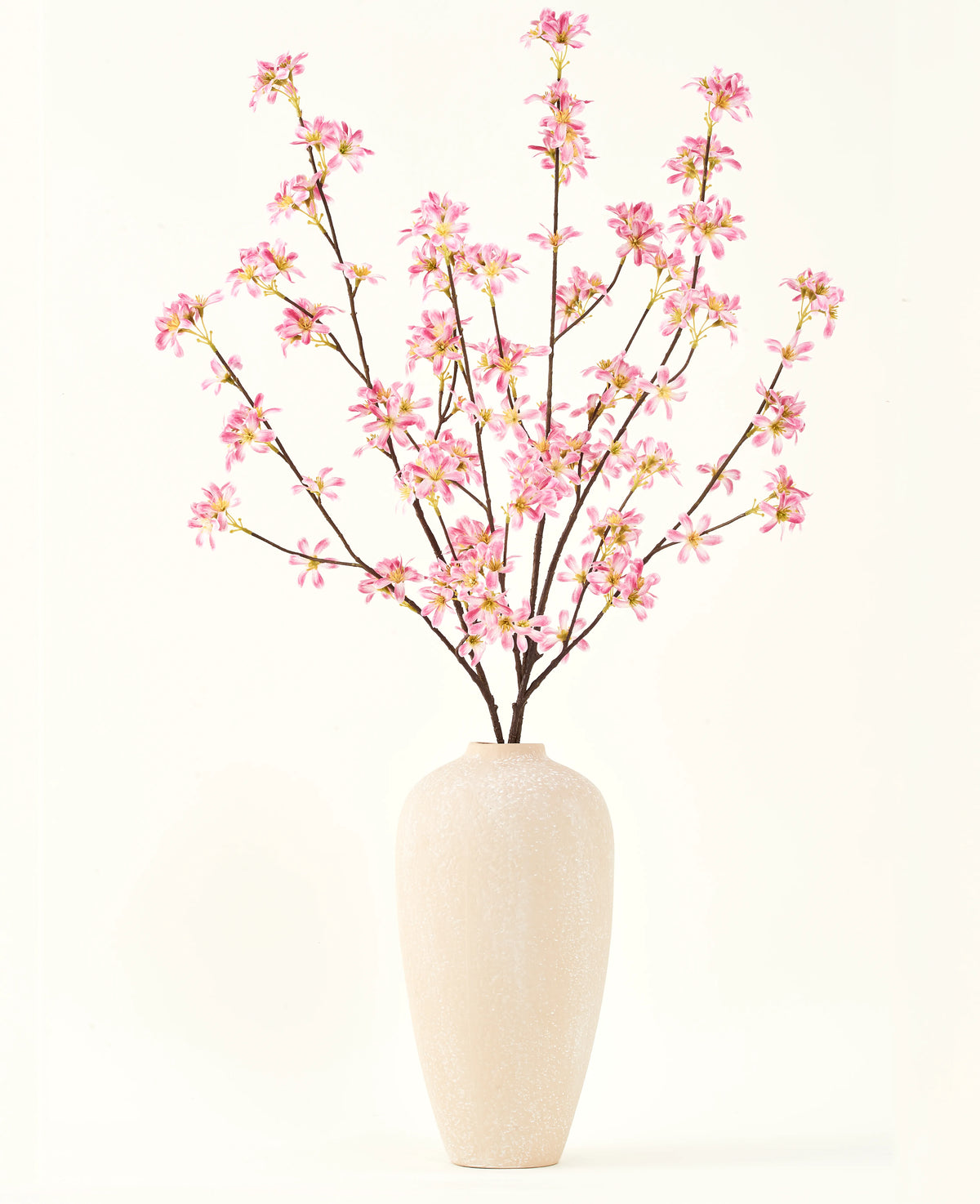 Een hoge vaas van beige keramiek bevat verschillende takken uit het Zijden kunstbloemen boeket Bloemen roze, met delicate roze bloesems en groene bladeren, tegen een effen witte achtergrond.