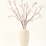 De Zijden kunstbloemen boeket Kersenbloesem blush 114 cm heeft hoge, delicate takken in een eenvoudige beige vaas, die een zachte, elegante touch toevoegt aan je interieur tegen een effen, lichte achtergrond.