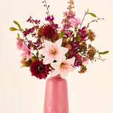 Een boeket van roze, bordeauxrode en witte Zijden kunstbloemen, het boeket Burgundy Dream, in een geribbelde roze vaas.