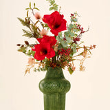 Zijden kunstbloemenboeket Christmas Elegance met rode amaryllis, eucalyptus en bessen in een groene keramische vaas met ribbels.