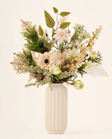 Zijden kunstbloemenboeket Golden Winter, bestaande uit kunstbloemen, bladgroen en een dennenappel in een geribbelde, gebroken witte vaas.