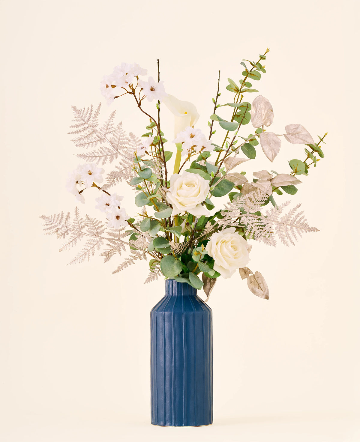 Zijden kunstbloemenboeket Silent Night, bestaande uit witte rozen en calla’s in een hoge, geribbelde blauwe vaas.