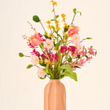 Zijden kunstbloemenboeket Spring Fling met gele forsythia, roze tulpen en kleine roze bloesems in een perzikkleurige geribbelde vaas.