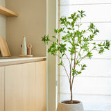 Een kunstplant Pieris Japonica van 150 cm staat bij een raam met doorschijnende gordijnen in een moderne, minimalistische keuken met lichte houten kasten en neutrale tinten.