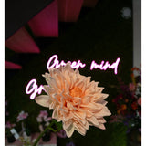 De Kunst Georgine Real Touch lichtroze bloem van 70 cm staat vooraan in focus, met een wazig neon "Open mind" roze cursief teken en verschillende bloemen en groen op de achtergrond.