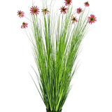 De Kunst Grasplant Chrysant 180 cm brandvertragend is een kunstplant in pot met hoge, dunne groene grasachtige bladeren en roze chrysantbloesems op lange stelen, afgebeeld tegen een witte achtergrond.