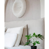 Een keurig opgemaakt bed met wit beddengoed staat naast een houten nachtkastje met de Kunst Pachira 30 cm plant. Boven het bed siert een wit gestructureerd cirkelvormig wandschilderij de lichtgekleurde muur.