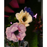 Close-up van drie Kunstanemoon Real Touch geel 52cm kunstanemoonbloemen - lavendel, crème en blauw - tegen vaag groen gebladerte en neonroze verlichting, met bloemstukken in de verte in beeld.
