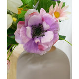 Close-up van de Kunstanemoon Real Touch paars 52cm, een lichtpaarse en roze bloem met een donker hart, omringd door groene bladeren en pastelkleurige bloemen in een mat witte vaas, tegen een zacht onscherpe achtergrond.